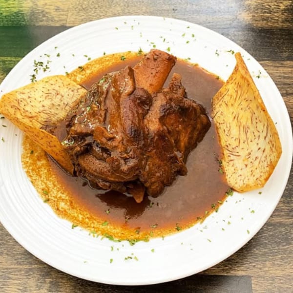 Cuban-style braised pork shank in a rich brown sauce, garnished with parsley and two taro chips.